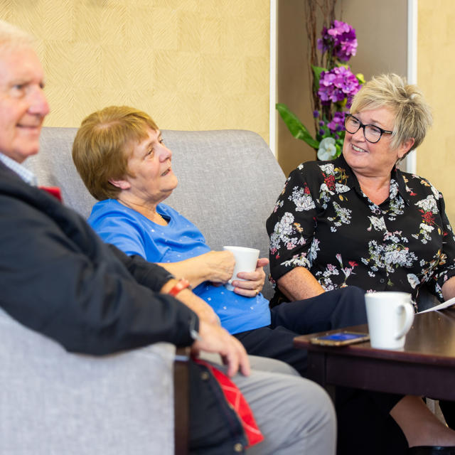 An older couple sat down talking to a member of staff over a cup of coffee