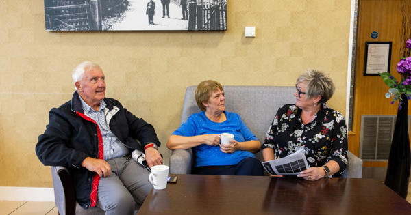 An older couple sat down talking to a member of staff over a cup of coffee