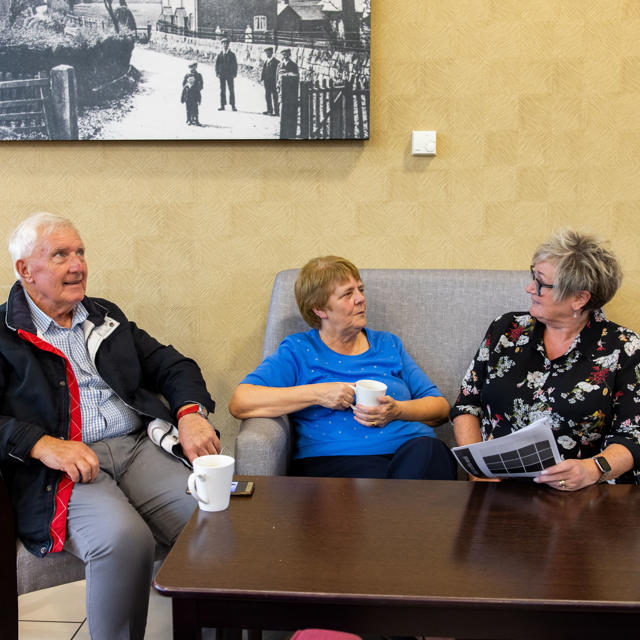An older couple sat down talking to a member of staff over a cup of coffee