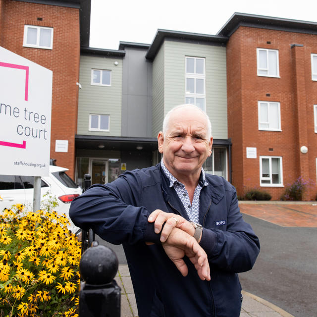 Older man standing in front of Lime Tree Court, a modern building signposted, with a smile on his face.